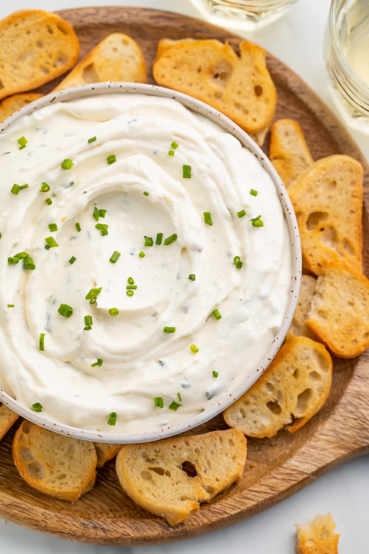 Creamy boursin dip in a bowl surrounded by crostini on a neutral platter.