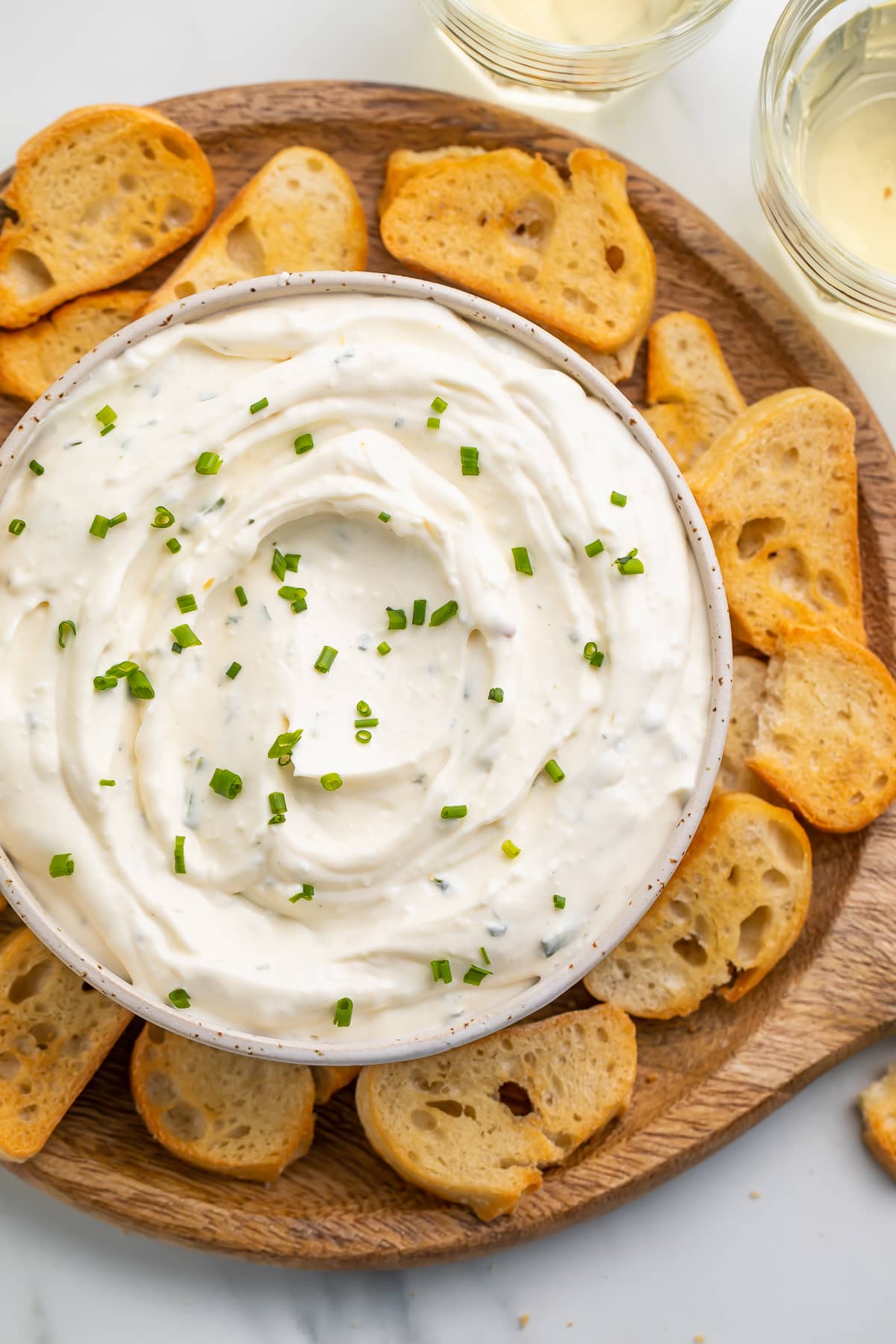 Creamy boursin dip in a bowl surrounded by crostini on a neutral platter.