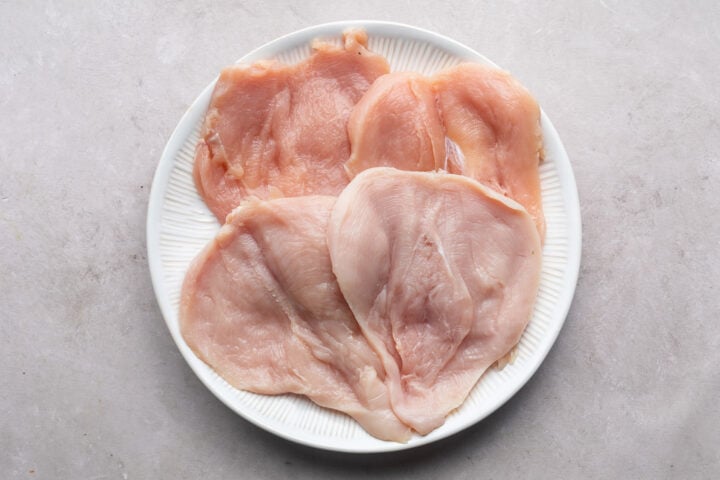 Butterflied chicken breasts on a round white plate.
