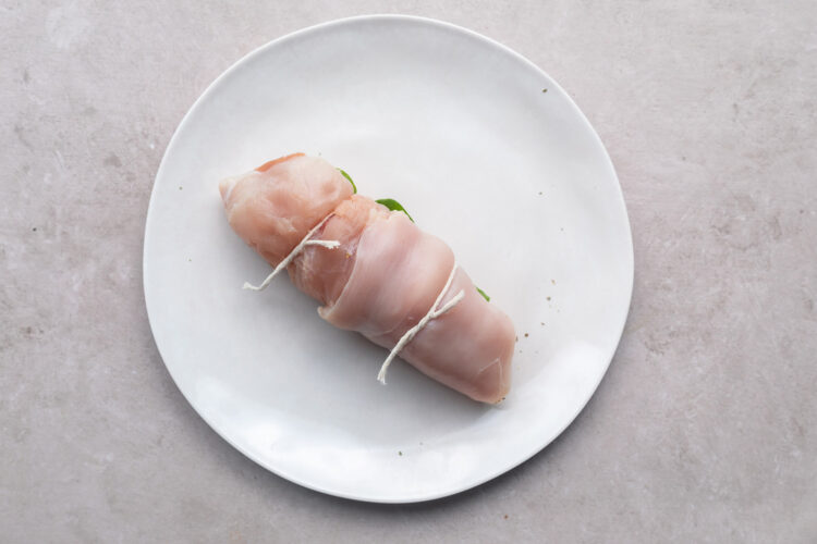 Chicken roulade tied with butcher's twine and resting on a white plate.