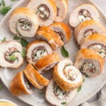 Several slices of chicken roulade, stuffed with prosciutto, spinach, and goat cheese, on a neutral plate.
