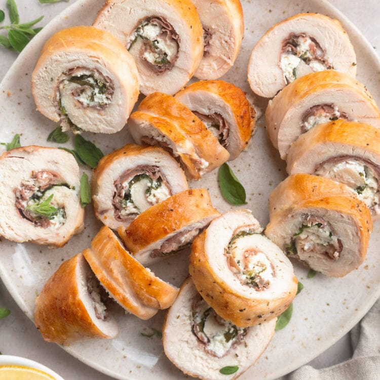 Several slices of chicken roulade, stuffed with prosciutto, spinach, and goat cheese, on a neutral plate.
