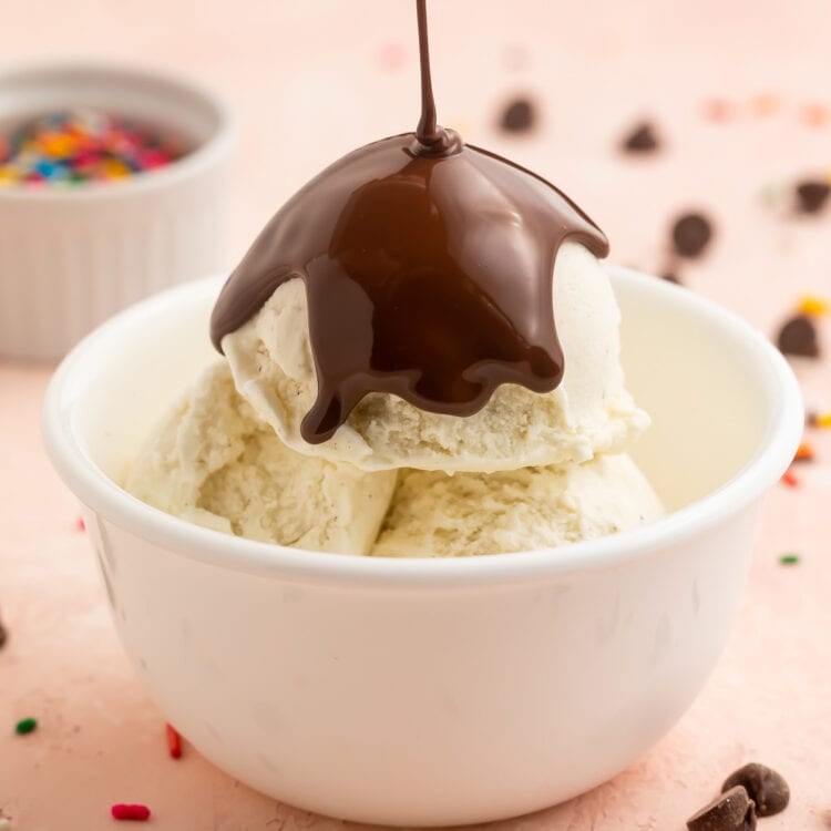 Chocolate keto magic shell being poured over a bowl of keto vanilla ice cream.