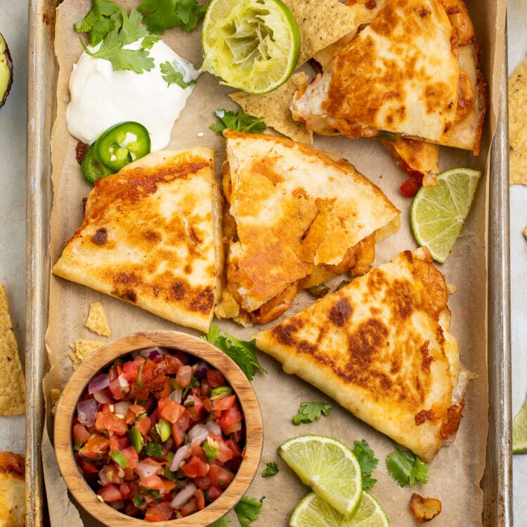 Overhead view of a shrimp quesadilla cut into 3 wedge-shaped slices surrounded by toppings.
