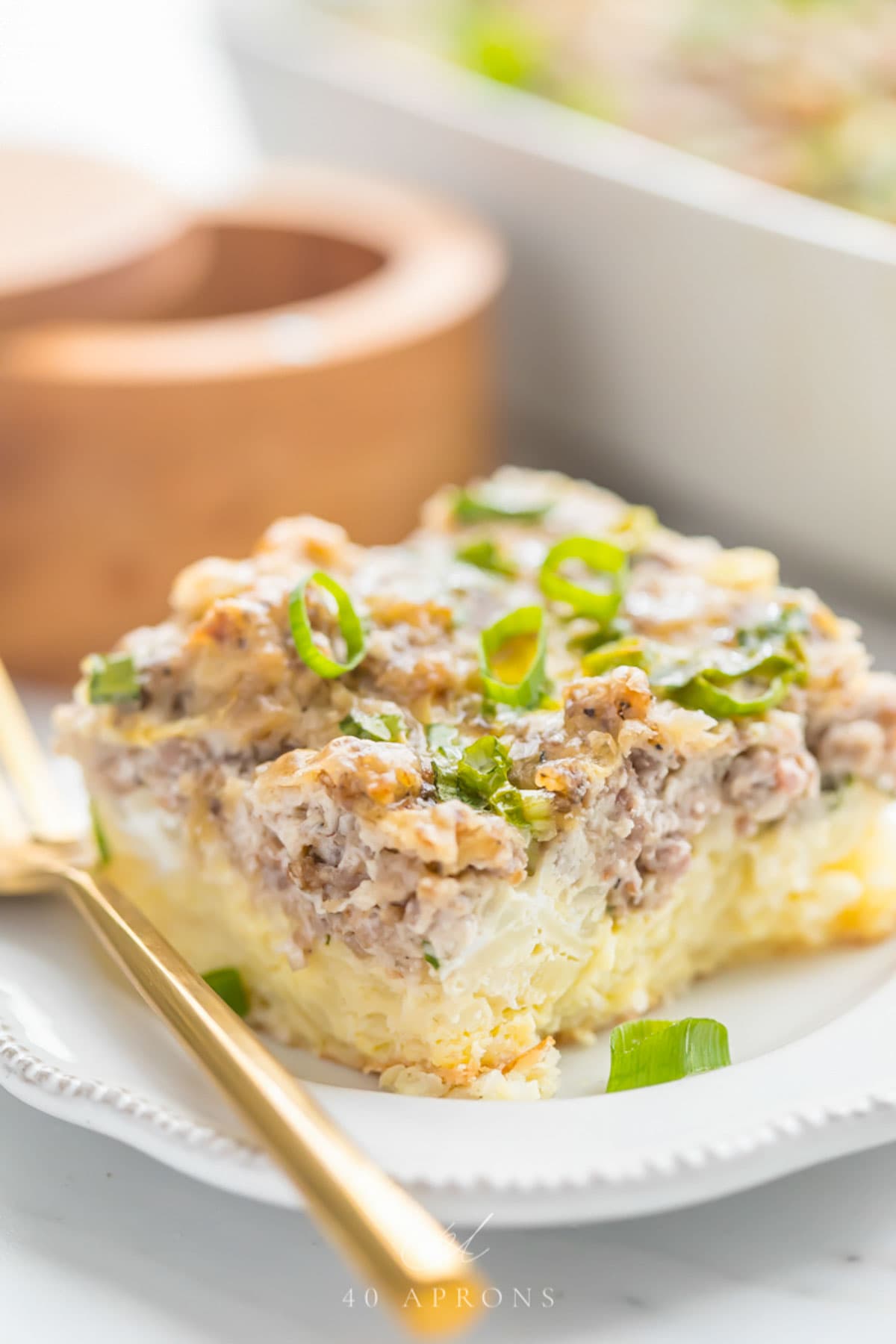 A square of Whole30 hashbrown sausage casserole on a plate with a gold fork.