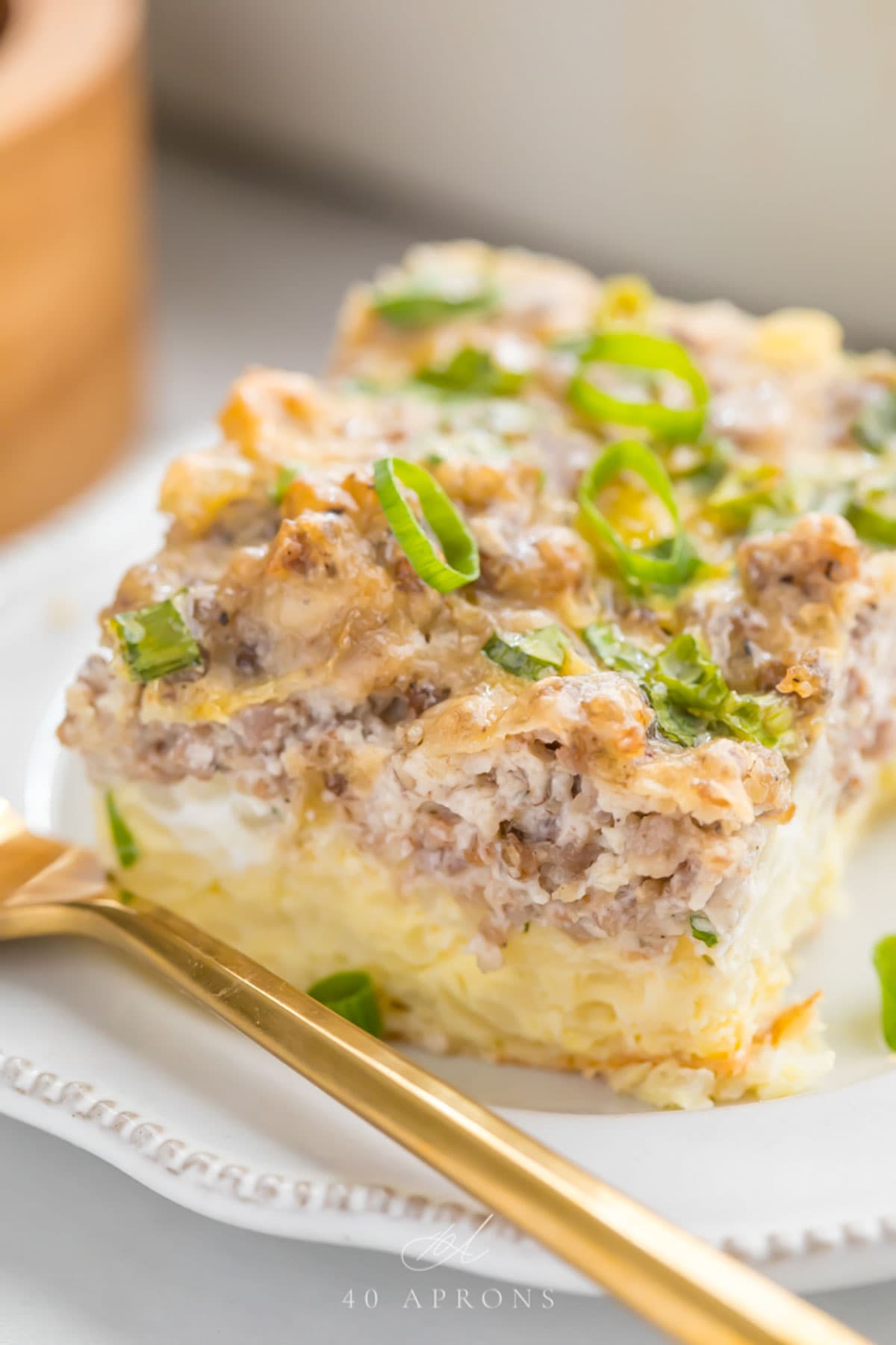 A square slice of a hashbrown breakfast casserole resting on a white plate with a gold fork.