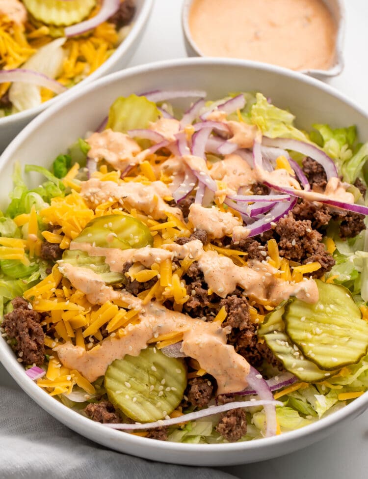 Angled view of a large Big Mac cheeseburger salad in a bowl with copycat Big Mac sauce in the background.