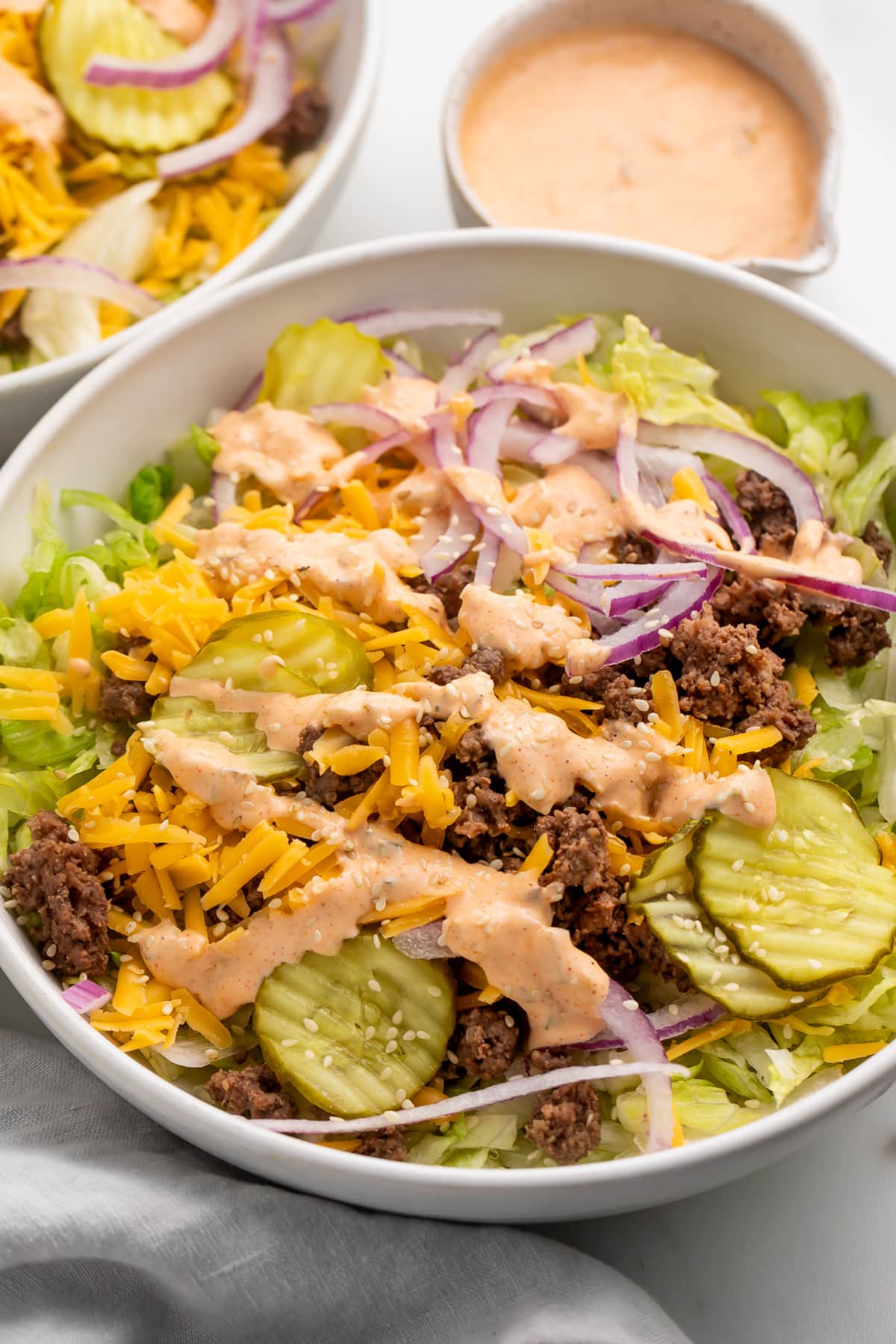 Angled view of a large Big Mac cheeseburger salad in a bowl with copycat Big Mac sauce in the background.