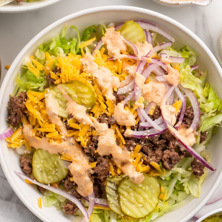 Top-down view of a large Big Mac cheeseburger salad in a bowl with copycat Big Mac sauce in the background.