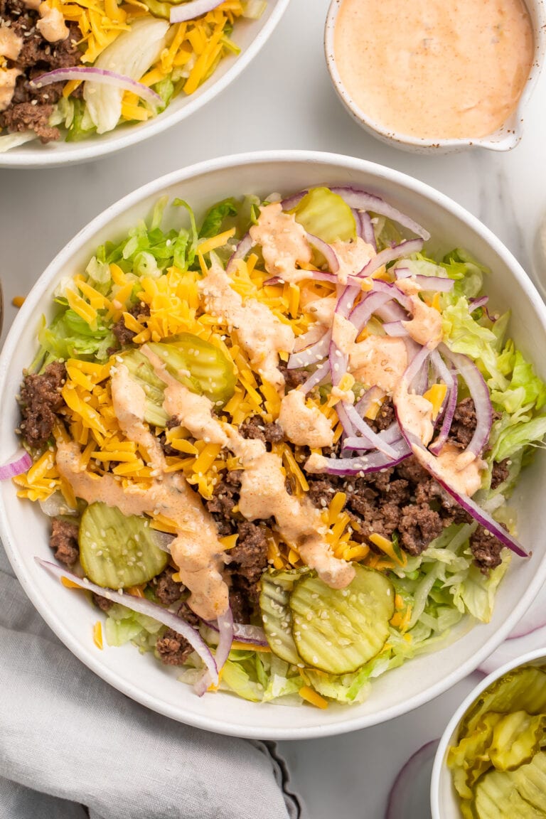 Top-down view of a large Big Mac cheeseburger salad in a bowl with copycat Big Mac sauce in the background.