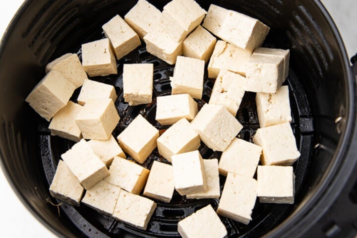 Uncooked cubes of tofu in a black air fryer basket.