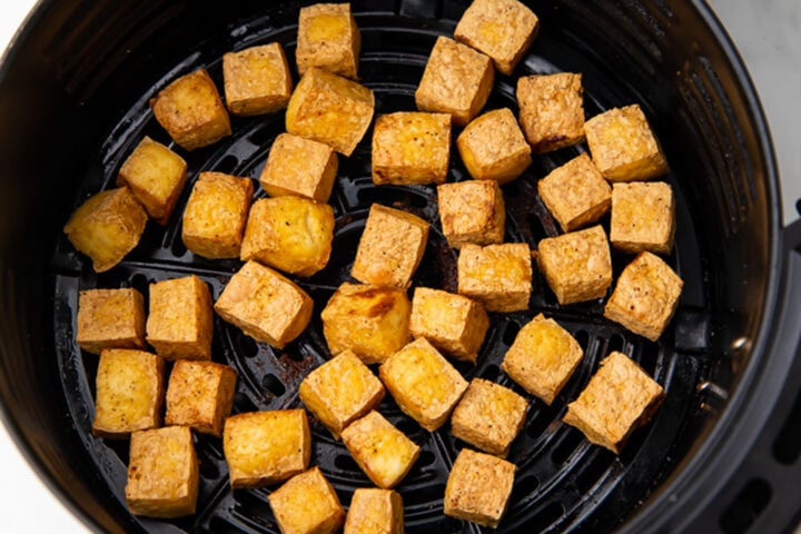 Air fried tofu cubes in a black air fryer basket.