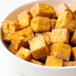 Cubes of crispy, marinated air fried tofu in a white bowl.