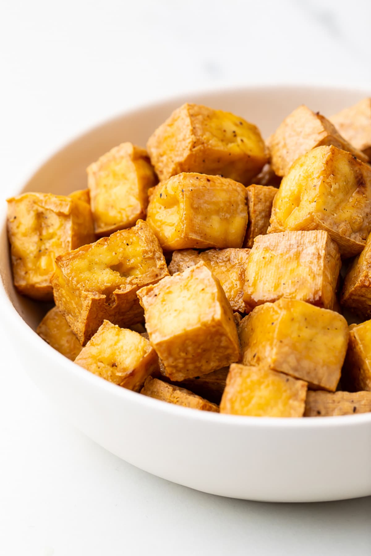 Cubes of crispy, marinated air fried tofu in a white bowl.