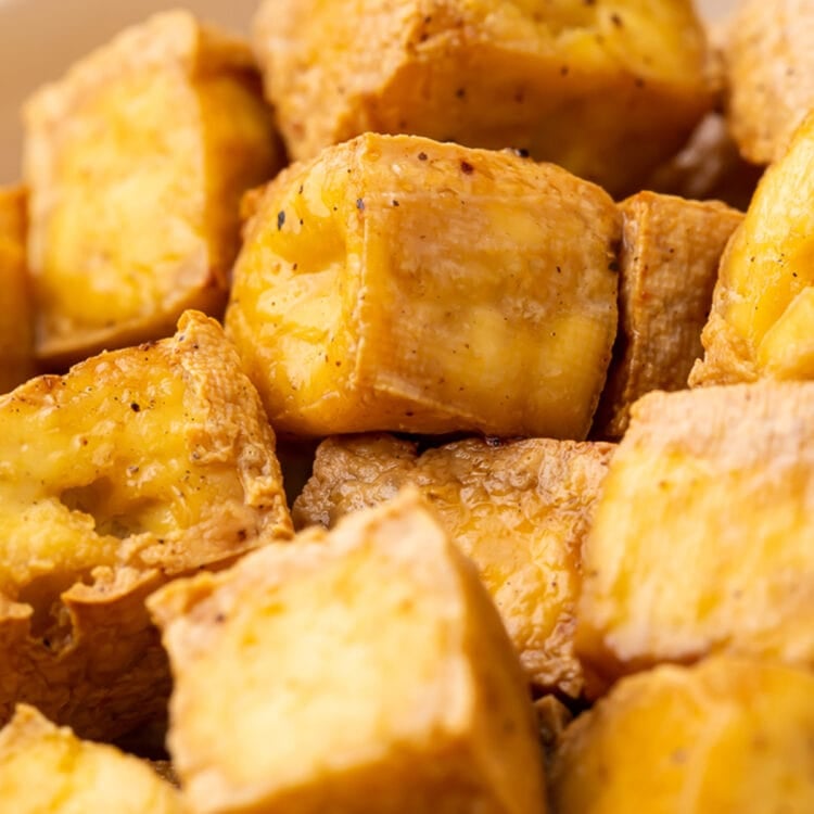 Cubes of crispy, marinated air fried tofu in a white bowl.