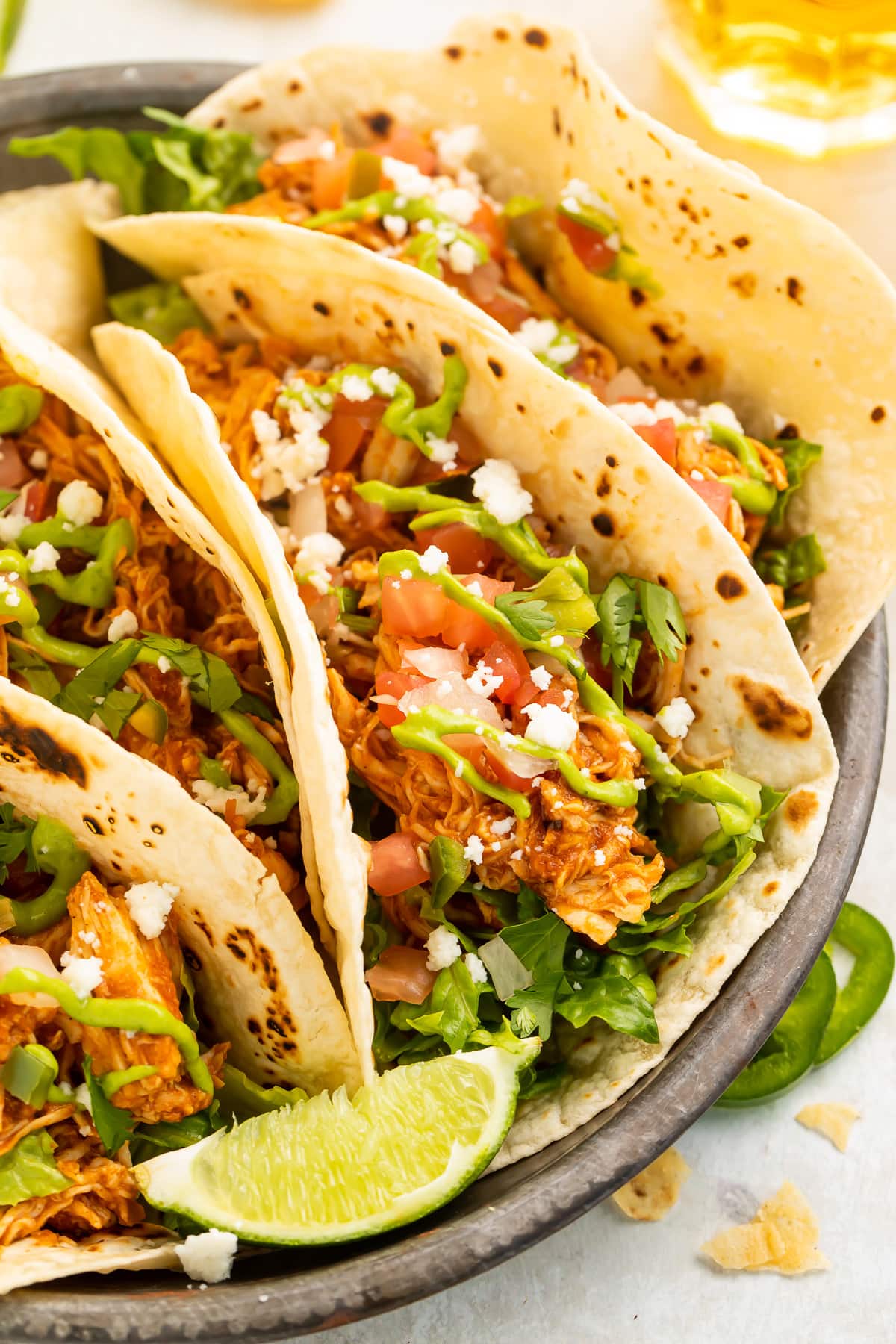 Close-up look at an Instant Pot chicken taco with shredded chicken, tomatoes, lettuce, cilantro, cheese, and a lime wedge.