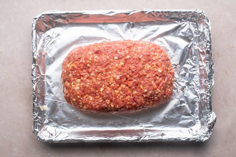 Ground beef mixture formed into loaf shape on a baking sheet lined with aluminum foil.