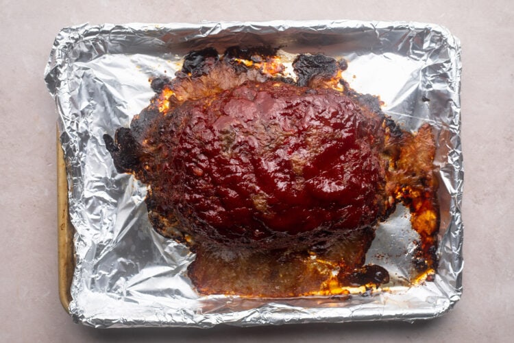 Baked gluten-free meatloaf topped with deep red ketchup glaze on a baking sheet.