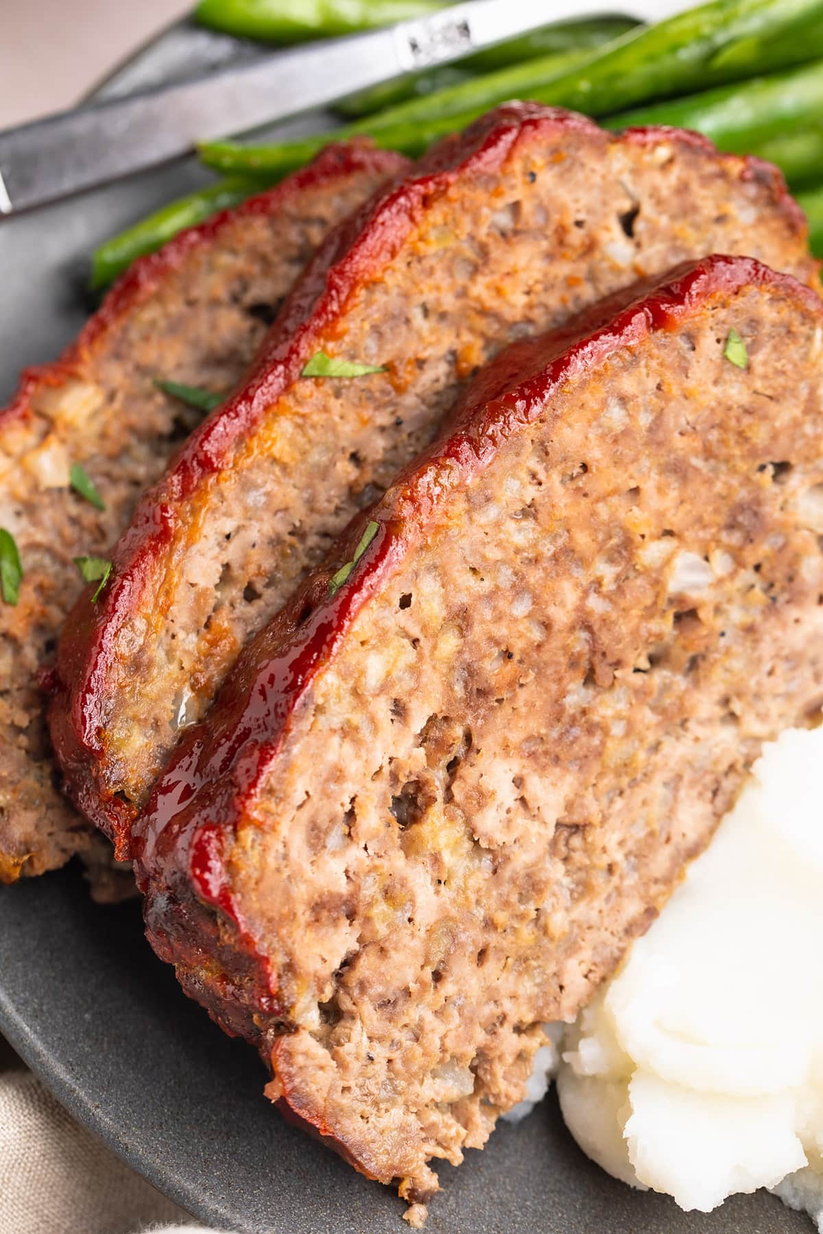 Close-up look at three slices of gluten-free meatloaf topped with red ketchup.