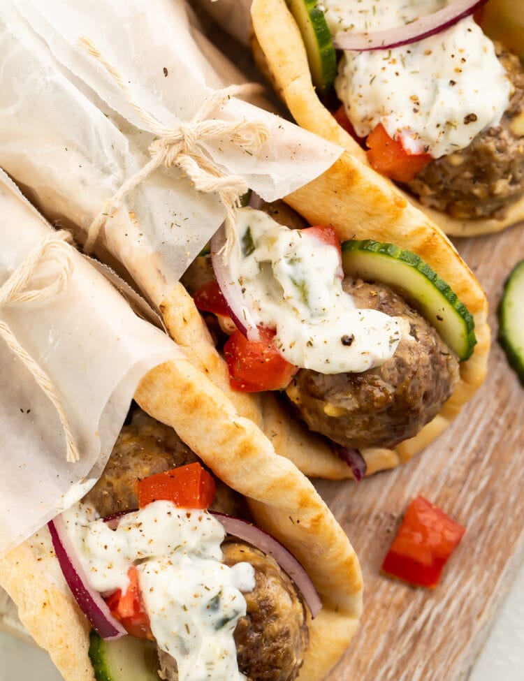 Three pitas stuffed with gyro meatballs, tzatziki, cucumber, and tomatoes, wrapped in parchment paper.