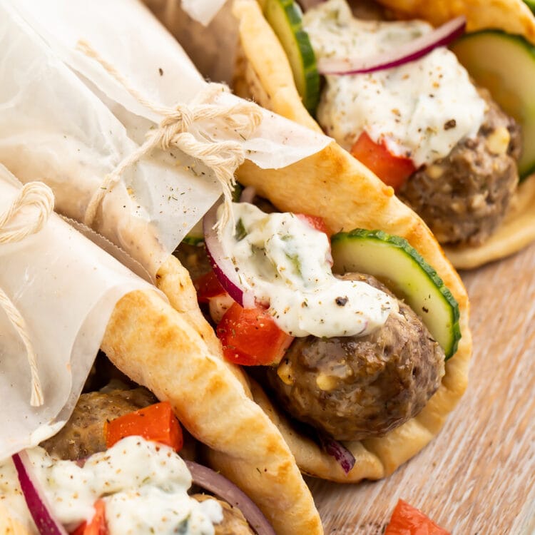 Three pitas stuffed with gyro meatballs, tzatziki, cucumber, and tomatoes, wrapped in parchment paper.