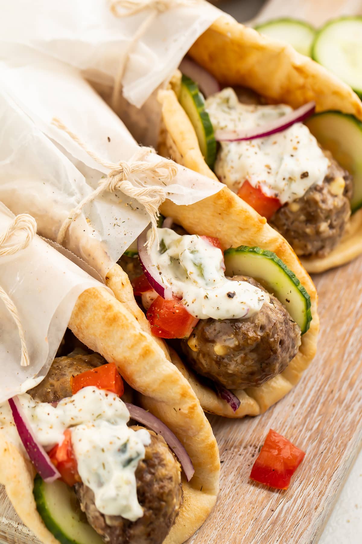 Three pitas stuffed with gyro meatballs, tzatziki, cucumber, and tomatoes, wrapped in parchment paper.