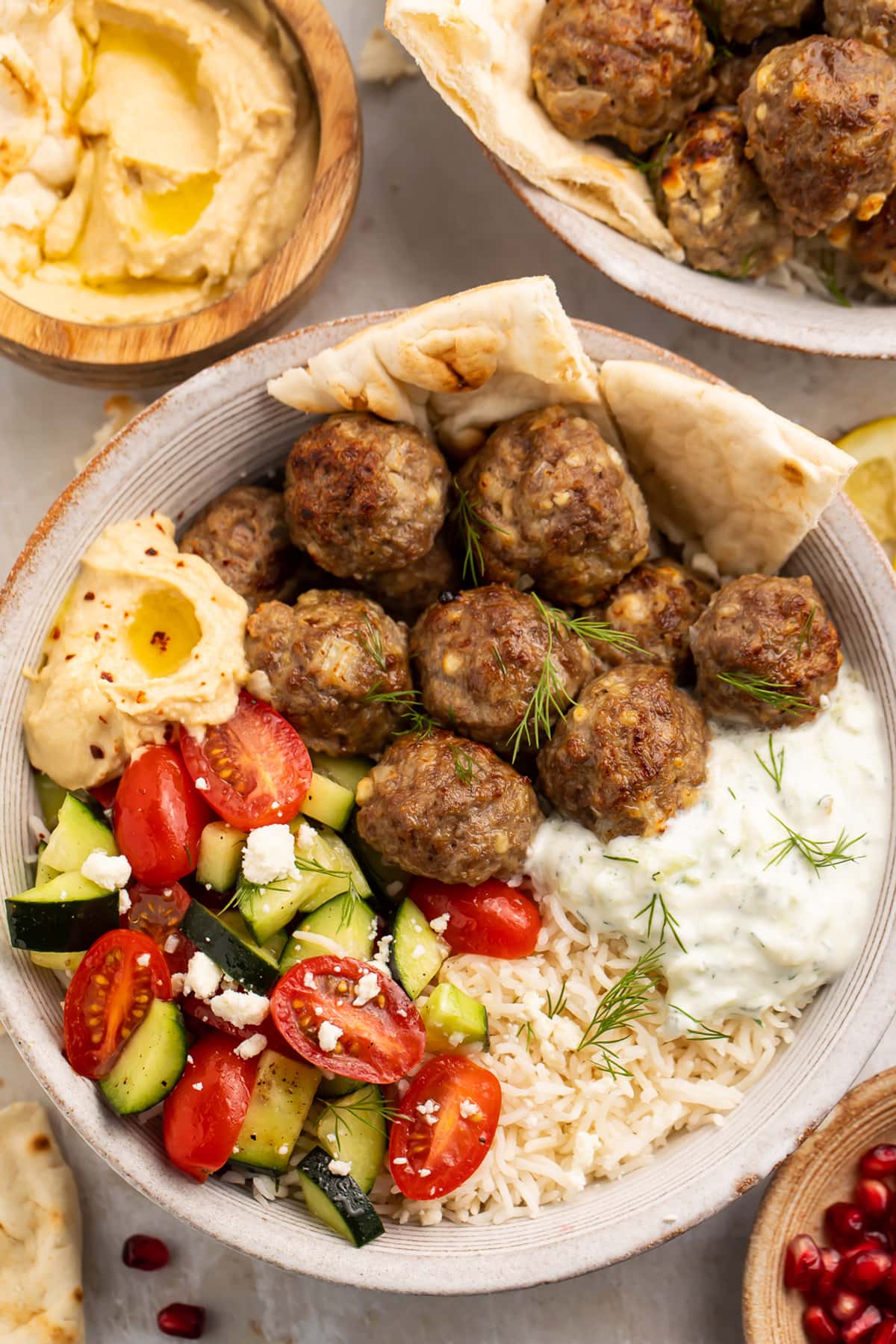 Gyro meatballs in a bowl with tomato and cucumber salsa, tzatziki, naan, and hummus.