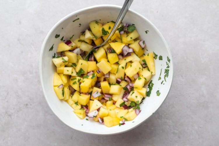 Mango salsa in a white bowl with a silver spoon.