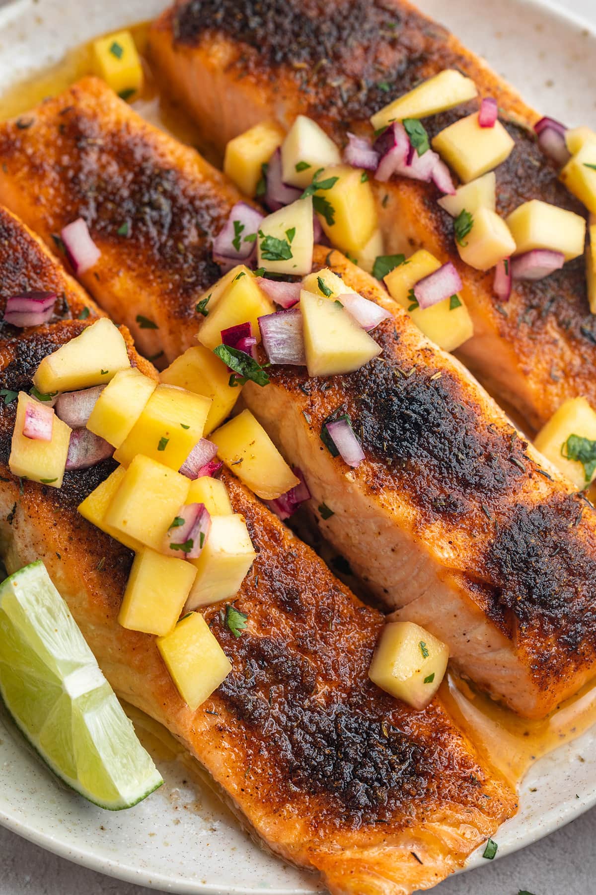 Three jerk salmon fillets topped with mango salsa on a round white plate.