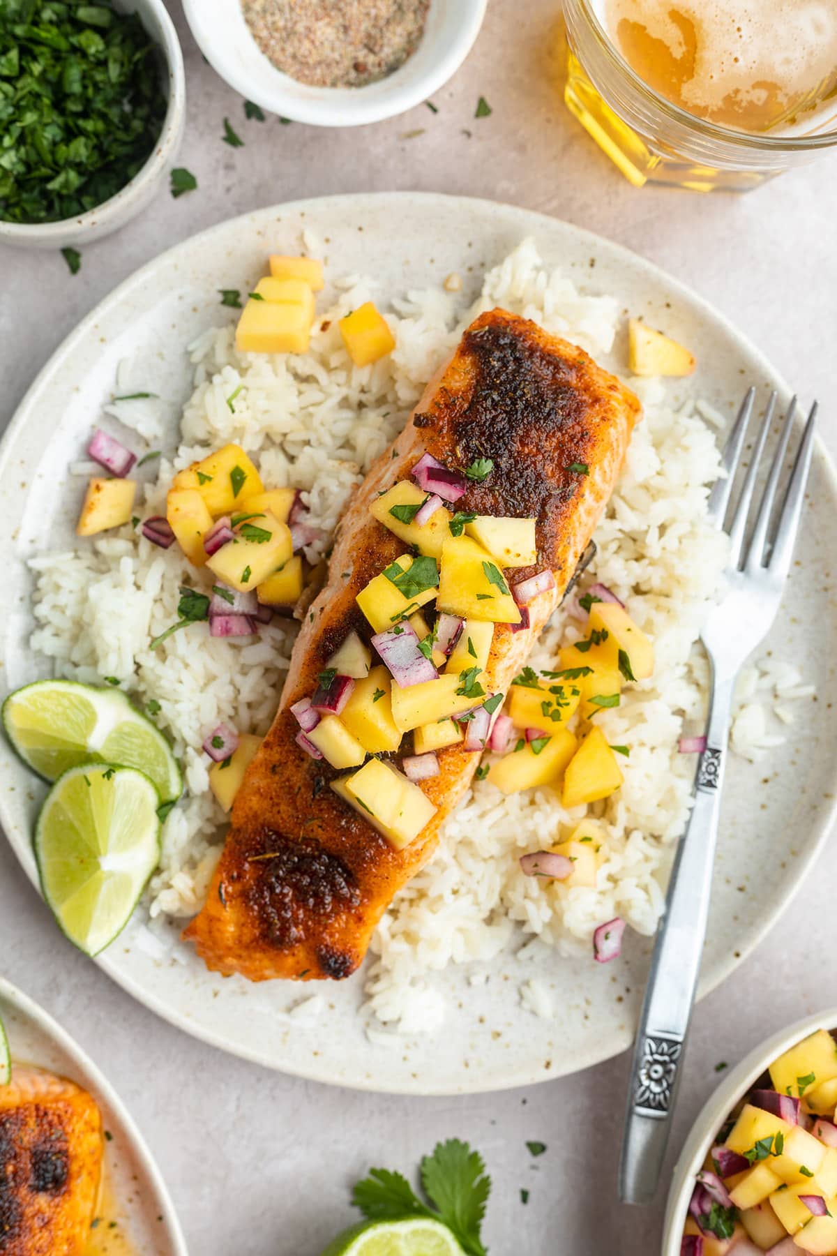 Jerk salmon topped with mango and red onion salsa on a plate with white rice and lime wedges.