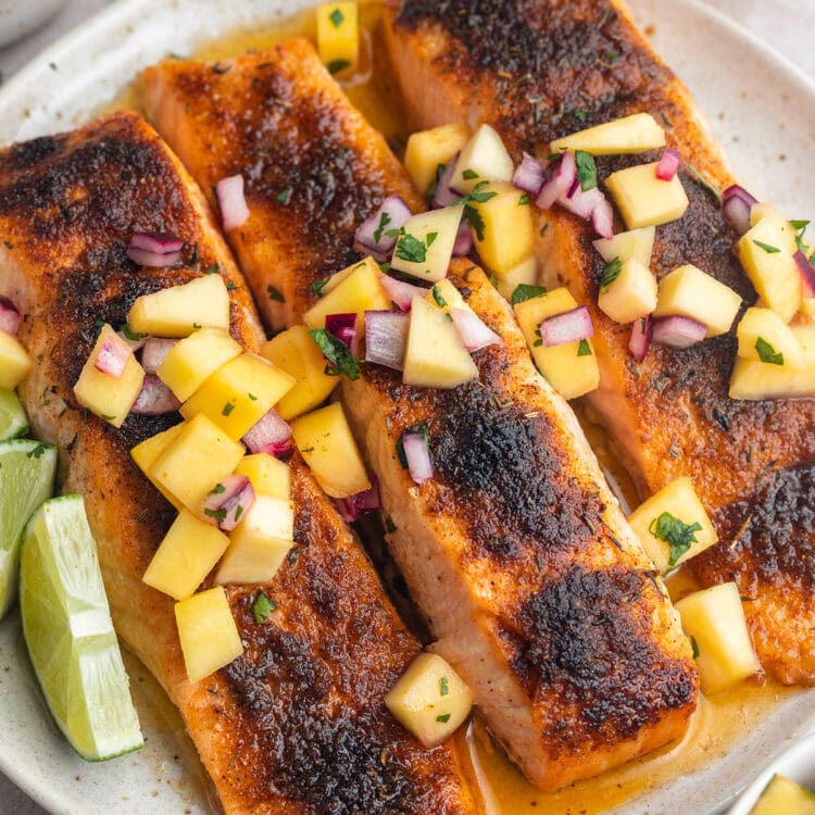 Three jerk salmon fillets topped with mango salsa on a round white plate.