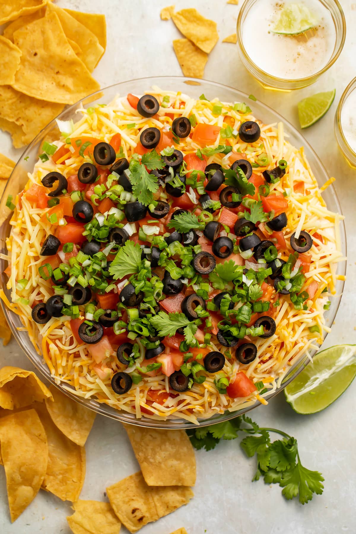 Top-down view of a large glass bowl of 7 layer dip topped with olives and green onions.