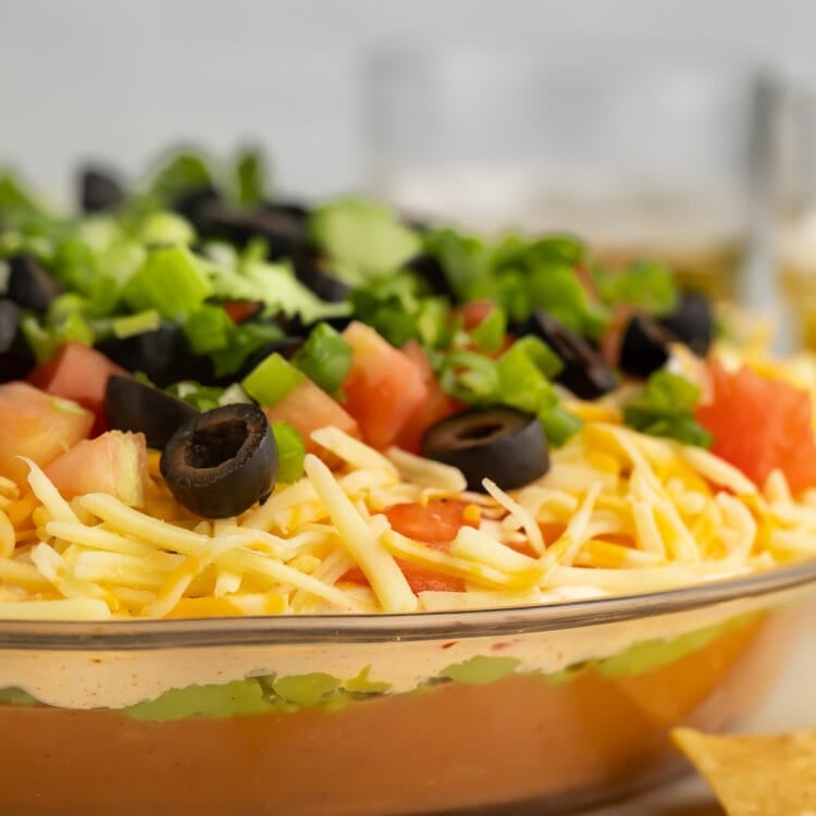 A side-view of a large glass bowl filled with a 7 layer dip.