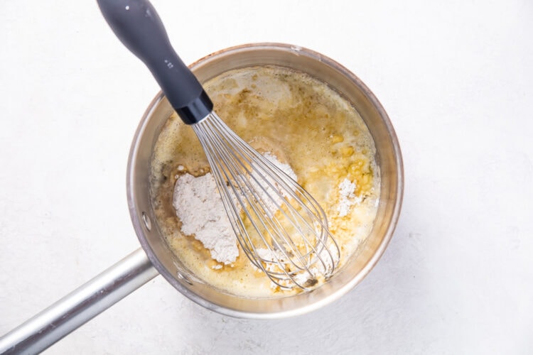 Melted butter and all-purpose flour in a silver saucepan with a silver whisk.