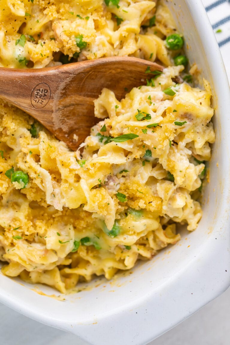 A large oval casserole dish holding tuna noodle casserole, with a large wooden spoon resting in the dish.