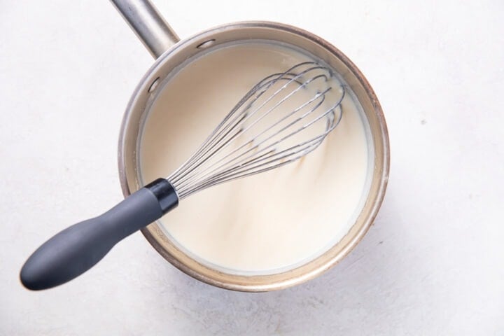 Roux base with 2 cups of whole milk in a silver saucepan with a wire whisk.