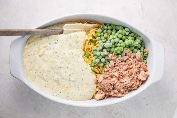 Separate components of tuna noodle casserole in a large white oval casserole dish.