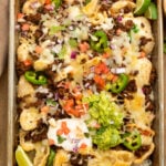 A sheet pan of loaded pork rind nachos topped with taco meat, guac, sour cream, tomato, and onions.