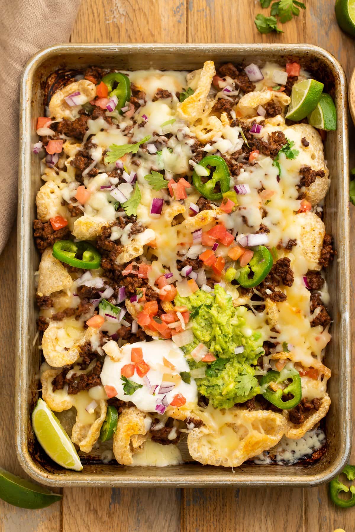 A sheet pan of loaded pork rind nachos topped with taco meat, guac, sour cream, tomato, and onions.