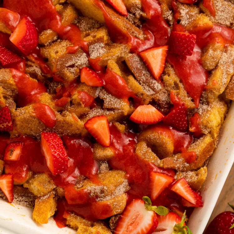 A casserole dish, angled on a table, filled with banana stuffed french toast casserole topped with strawberries.