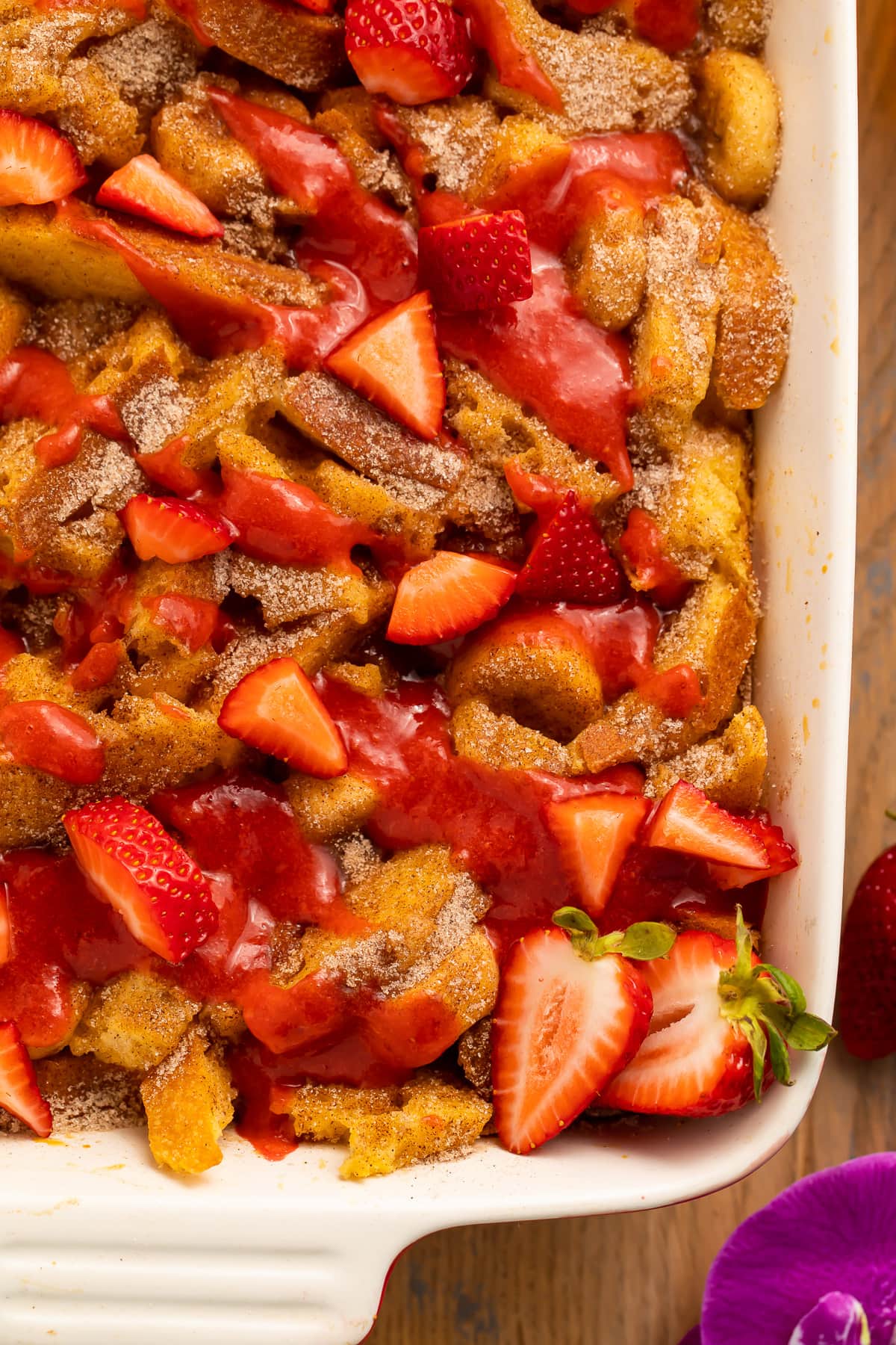 A casserole dish, on a table, filled with banana stuffed french toast casserole topped with strawberries.
