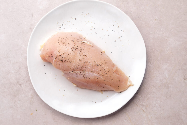 Seasoned chicken breast on a large white round plate.