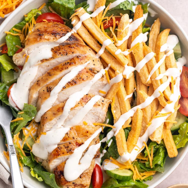 Zoomed out, top-down view of a Pittsburgh salad topped with sliced chicken, french fries, and ranch dressing.
