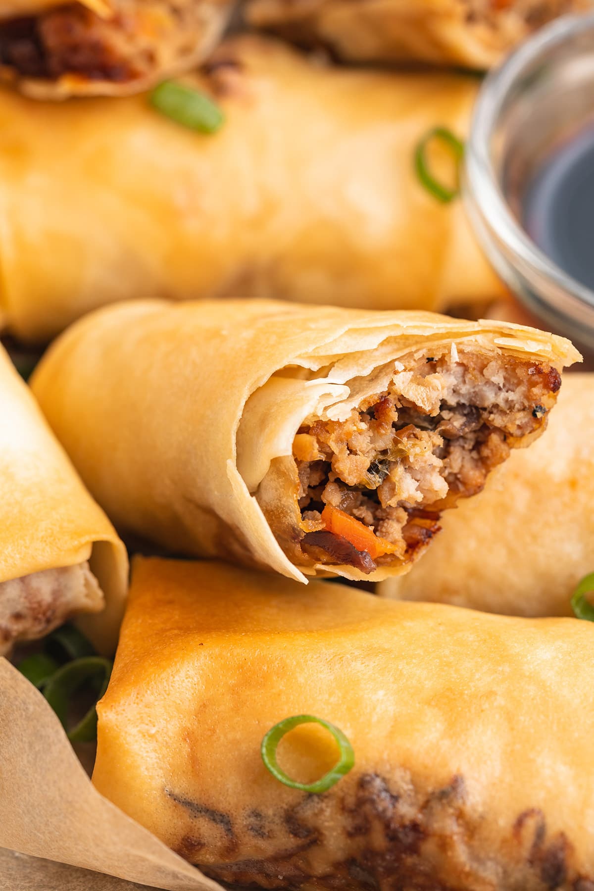 Close-up of a homemade air fryer egg roll, with one bite taken out of the end closest to the camera, showing the pork and veggie filling.