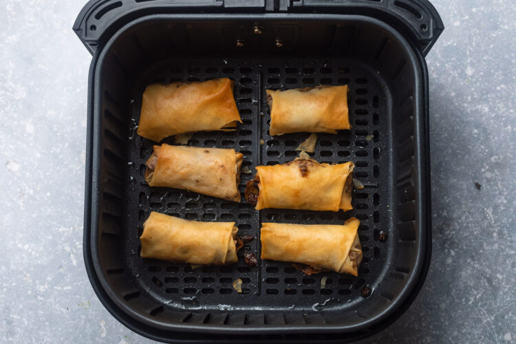 Six homemade pork egg rolls placed horizontally in two columns in a black air fryer basket.