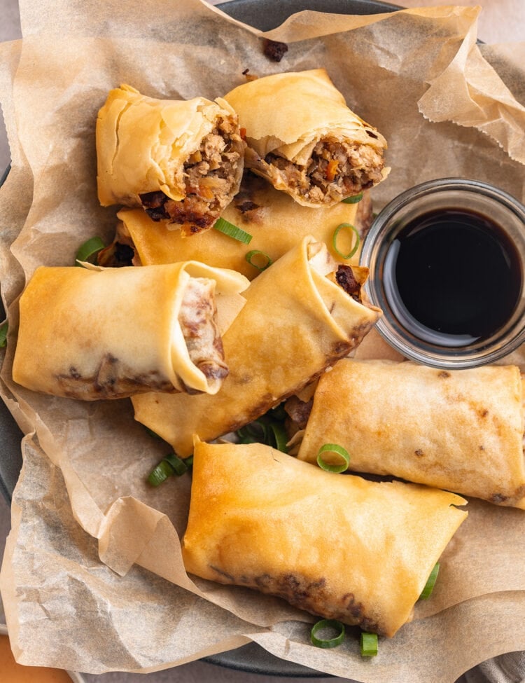 Top-down, overhead view of homemade air fryer egg rolls on a plate lined with parchment paper next to a small bowl of soy sauce.
