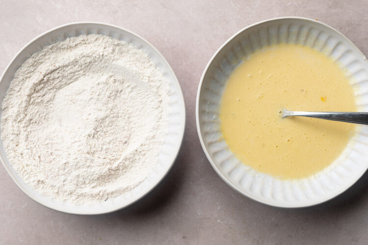 Seasoned flour breading mixture on a shallow bowl on the left, and pale yellow egg and milk mixture in a shallow bowl on the right.