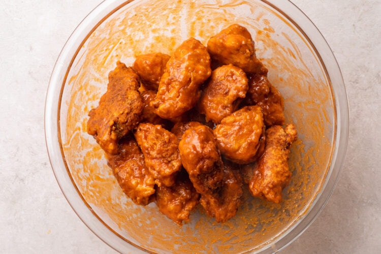 Breaded, fried boneless chicken wings with buffalo sauce in a large glass mixing bowl.