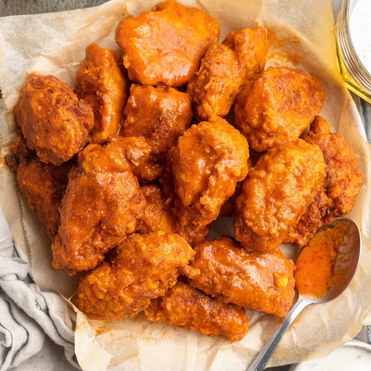 Top-down view of a large bowl, lined with parchment paper, holding several orange-sauced buffalo chicken wings.