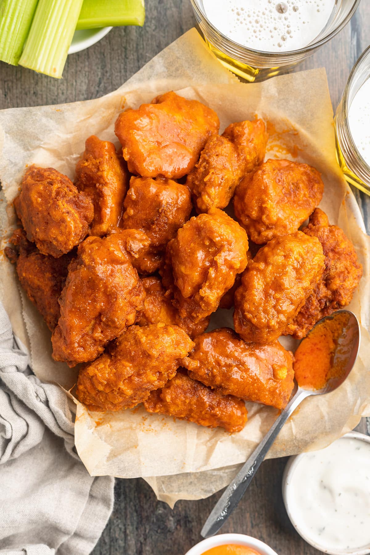 Top-down view of a large bowl, lined with parchment paper, holding several orange-sauced buffalo chicken wings.